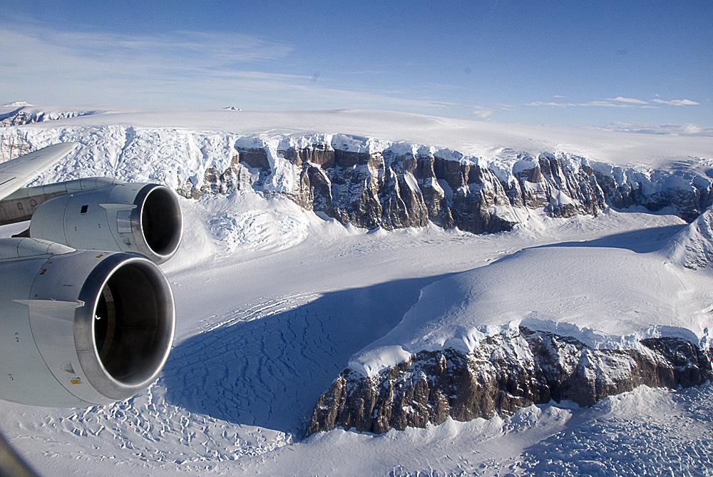 Airplane wing and engine over a snow covered valley